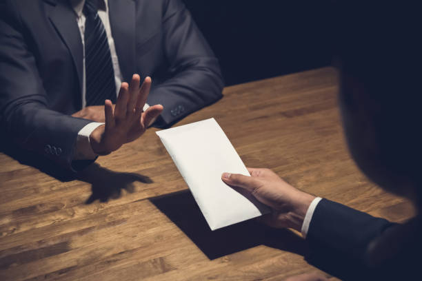 Businessman rejecting money in white envelope offered by his partner in the dark - anti bribery concept